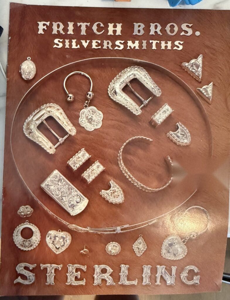 Catalog-era display board of Fritch Bros. sterling buckle sets, money clip, bracelet, collar tips and charms on a hide background