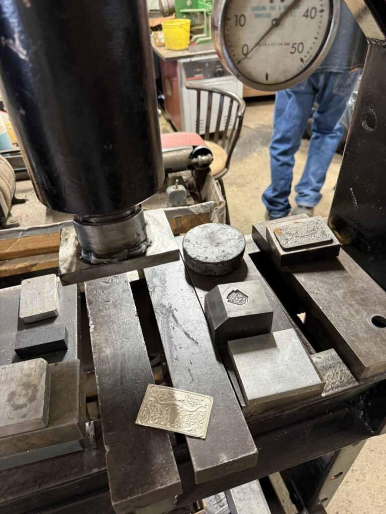 Dies and a stamped silver blank on the bed of a press in the Fritch Brothers workshop